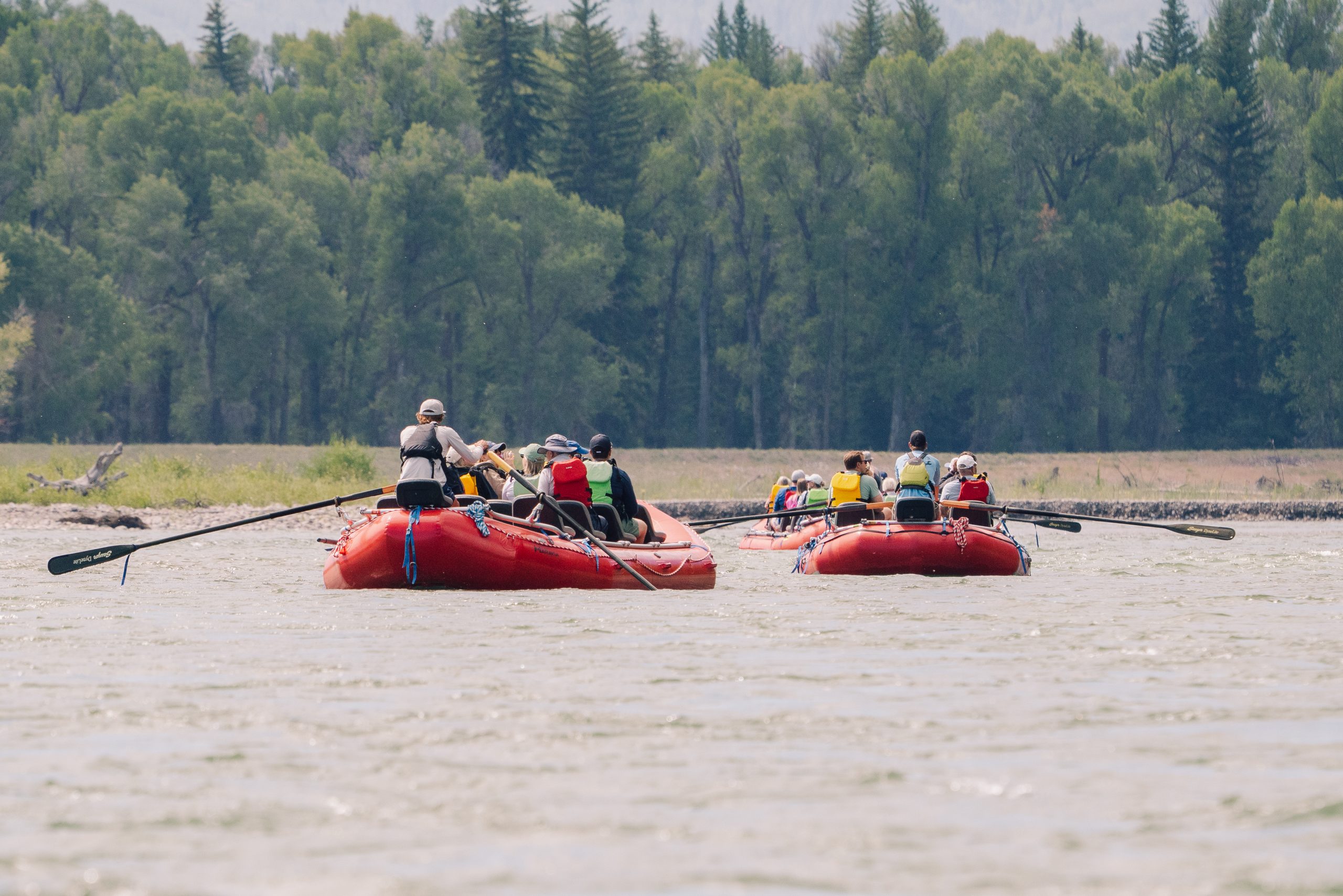 2 red snake river float tour rafts floating down the river with trees in the background.